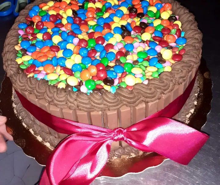 Bolo cercado de biscoitos de chocolate, coberto de confeitos coloridos e laço pink