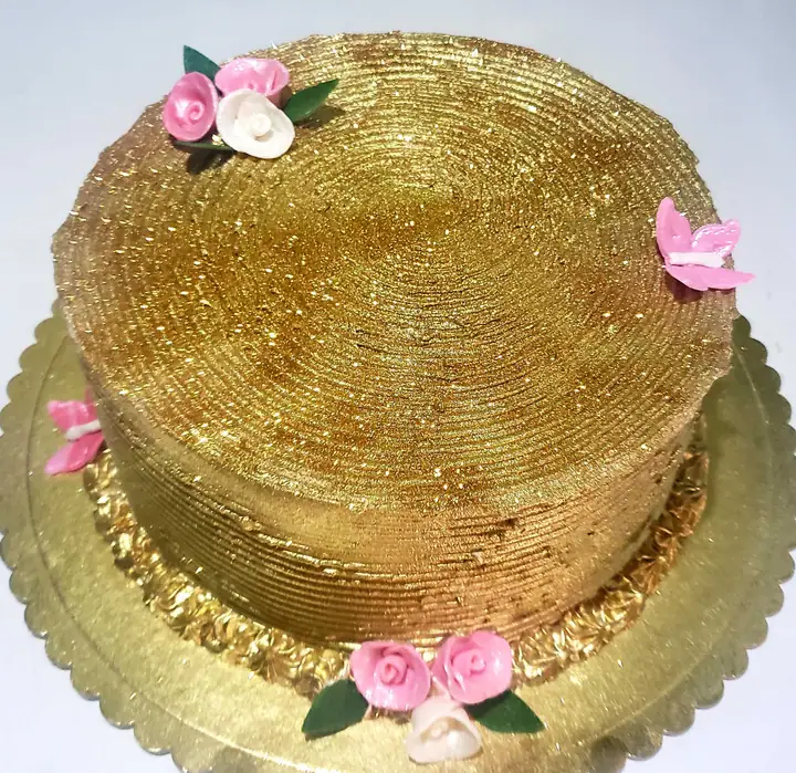 Bolo redondo com cobertura dourada brilhante e flores rosa