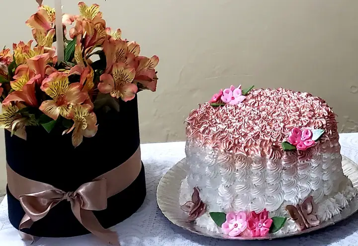 Bolo branco com rosetas cor-de-rosa e flores ao lado de arranjo floral