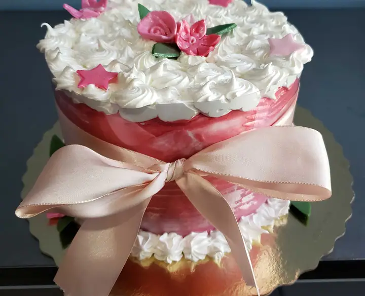 Bolo com faixa rosa, laço de cetim e flores de merengue