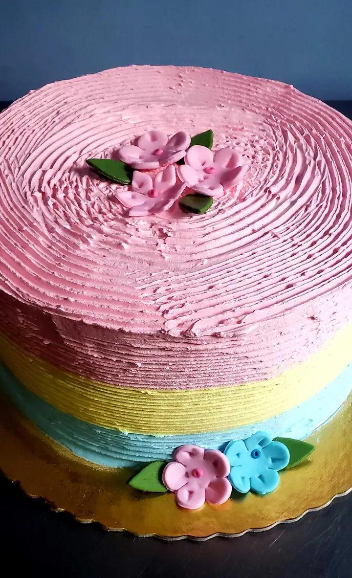 Bolo em faixas de merengue rosa, amarelo e azul com flores