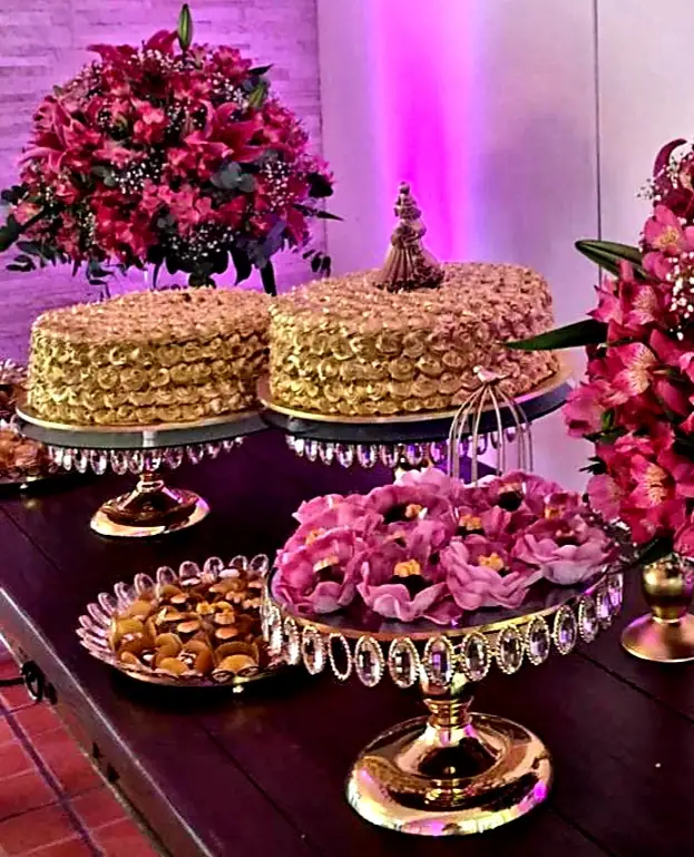 Mesa com bolos de merengue dourado em boleiras de cristal e flores pink