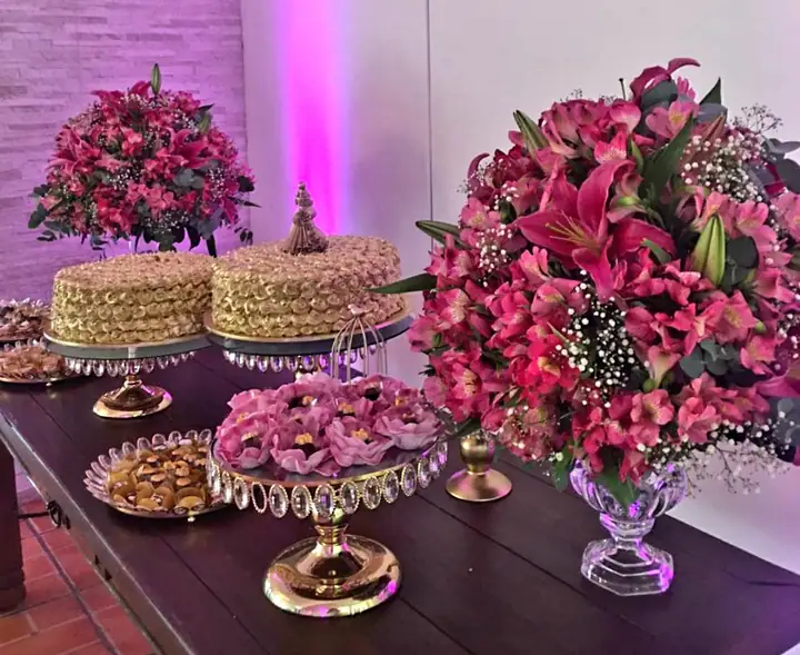 Mesa de festa com dois bolos de merengue dourado, doces e arranjos de lírios